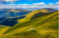 stone among the grass on top of the hillside meadow near the edge of a mountain hill. vivid summer landscape.