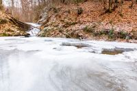 winter landscape with forest and frozen river. tranquil scene with beech trees near the shore of ice covered water stream through carpathian mountains. beautiful weather background or travel concept
