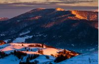 beautiful warm winter sunrise on cloudy morning in snow covered fields near rural area of Carpathian mountains
