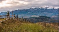 wooden fence on hills of mountainous countryside. agricultural fields in late autumn gloomy weather. mountain ridge with snowy tops in the distance