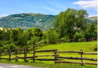 composite image of wooden fence on agricultural grassy meadow with trees on hillside in high mountains