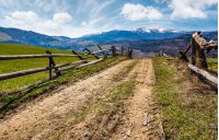 wooden fence on rural hill in spring. lovely mountainous landscape with snowy peaks in the distance