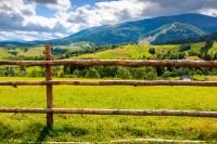wooden fence on the grassy meadow in mountainous countryside. rural landscape of transcarpathia with rolling hill in september on a sunny day with clouds on the blue sky