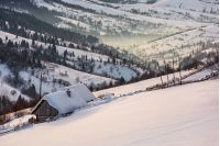 woodshed on hillside in deep snow. beautiful winter rural scenery in the mountainous village outskirts at foggy sunrise
