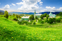 Composite image of green Monastery in mountains on hillside with grass and dandelions in morning light